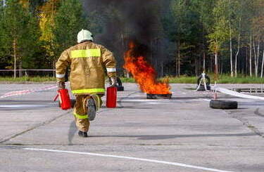 Ćwiczenia strażackie, strażak biegnie gasić ogień z dwoma gaśnicami.